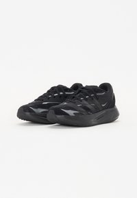Baskets noires de sport avec une tige en mesh, des panneaux texturés et une semelle noire rembourrée. Lacets et accents de marque dans des tons sombres.