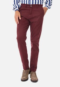 Chinos bordeaux in cotone con una texture liscia, dotati di chiusura a pulsante e tasche laterali, abbinati a stivali marroni con lacci.