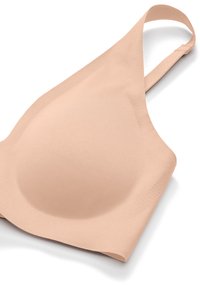 Reggiseno wireless beige senza cuciture con coppe sagomate e spallina regolabile, disteso su una superficie bianca.