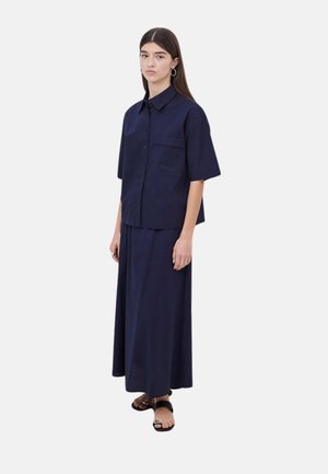 Camisa de manga corta de color azul marino con bolsillo frontal, combinada con una falda larga a juego. Tejido suave y diseño sencillo. Sandalias negras.