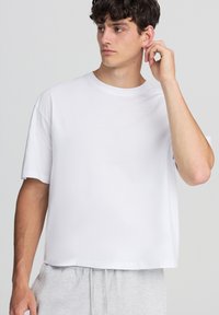 Biała bawełniana koszulka, krótki rękaw, okrągły dekolt, luźny krój, gładka faktura, w połączeniu z jasnoszarymi dresami, minimalistyczny design.