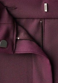 Tejido burdeos con una textura suave que cuenta con una cremallera y un acento plateado. El diseño incluye una solapa plegada y detalles de costura.