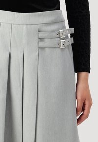 Jupe gris clair avec un motif en chevrons, des plis sur le devant et deux sangles latérales avec des boucles en argent pour la fermeture et l'ajustement.