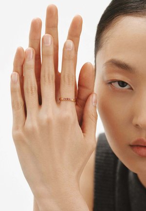 Anillo de oro con cinco pequeñas gemas de colores, exhibido en una mano con una textura suave y un acabado de uñas natural, sobre un fondo liso.