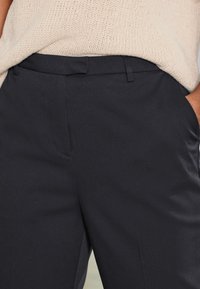 Tamsiai mėlynos, prigludusios kelnės su lygiu tekstūru, turinčios šonines kišenes ir lygų priekinį dizainą. Puikiai dera su įvairiais viršutiniais drabužiais.