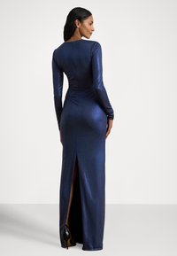 Vestido de noite azul-marinho com mangas compridas, silhueta elegante e racha nas costas. Feito de um material brilhante e suave com um ligeiro brilho.