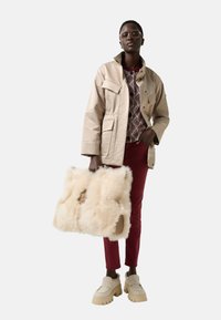 Beige waterproof jacket with pockets, burgundy pants, and cream faux-fur bag. Chunky beige shoes. Geometric patterned top underneath.