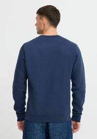 Felpa blu navy con colletto tondo, maniche lunghe e polsini a costine. Texture morbida e vestibilità rilassata, con un dettaglio di cucitura sul retro.