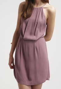 Robe sans manches violette avec un devant drapé, tissu texturé et taille ajustée. Légère et fluide, atteignant le milieu de la cuisse.