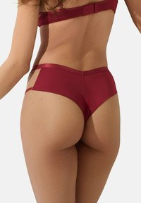 Culotte taille haute bordeaux avec une texture lisse et des panneaux latéraux transparents, présentant un design sans coutures et une taille douce et brillante.