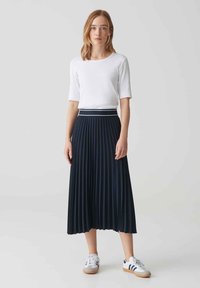 Jupe midi plissée bleu marine avec une ceinture élastique blanche, assortie à un haut blanc ajusté et des baskets blanches avec des rayures bleu marine.
