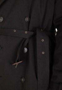 Cappotto lungo nero con design doppiopetto, grandi bottoni, vita con cintura e occhielli, e tessuto testurizzato.