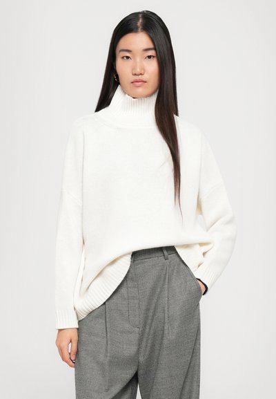 Vit, ribbad polotröja med oversize passform, kombinerad med högtalande grå houndstooth-byxor med veck och sidofickor.
