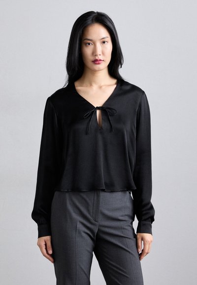 Black blouse with a V-neck and tie detail at the front; long sleeves; smooth texture; paired with gray tailored pants.