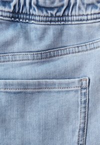 Tessuto di denim azzurro con vita elastica e cuciture visibili, caratterizzato da una tasca posteriore rettangolare sui jeans.