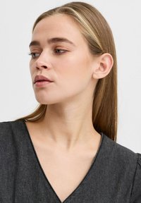 Haut gris foncé à col en V avec des manches courtes bouffantes. Tissu doux et léger avec une texture lisse. Gros plan du visage, montrant un maquillage neutre et des cheveux raides.