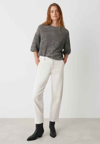 Grauer strukturierter Strickpullover mit kurzen Ärmeln, kombiniert mit weißen geraden Hosen und schwarzen Knöchelstiefeln, die ein lässiges Ensemble bilden.