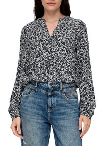 Dunkelblaue Bluse mit weißem Blumenmuster, langen Ärmeln und V-Ausschnitt, kombiniert mit hochtaillierten, ausgewaschenen blauen Jeans.