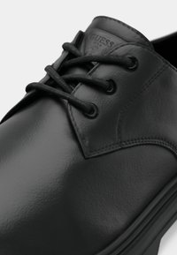 Sapato preto de couro com acabamento liso, biqueira arredondada e design de atacadores com seis ilhós. Apresenta um pequeno logótipo em relevo na língua.