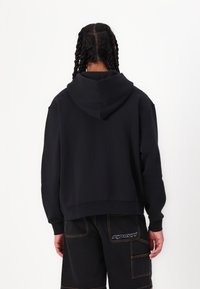 Schwarzer Hoodie aus weichem Stoff, mit einer Kordelzugkapuze, lockerer Passform und gerippten Bündchen. Die Rückseite zeigt ein einfaches Design ohne Grafiken.