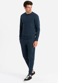 Conjunto de sudadera y pantalones deportivos en azul marino, fabricado con un tejido suave, con puños y cintura acanalados, con un ajuste holgado y un diseño minimalista.