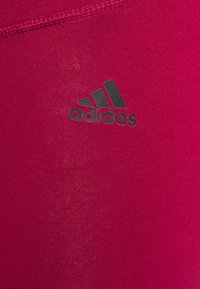 Leggings atléticos cor-de-rosa com uma textura lisa e elástica; apresentam um logo preto da Adidas no lado superior esquerdo.