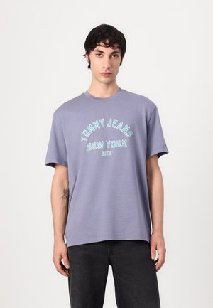 Violet medvilninė marškinėliai su apvalia kaklo išpjova ir trumpomis rankovėmis. Turkuos tekstas rašmenimis sako "TOMMY JEANS NEW YORK CITY."