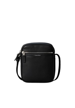 Schwarze perforierte Crossbody-Tasche mit vorderer Reißverschlusstasche und verstellbarem Riemen, Calvin Klein Logo-Plakette mittig unter dem Reißverschluss.