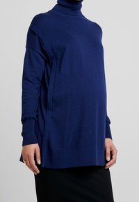 Dunkelblauer Rollkragenpullover, weicher Stoff, lockerer Schnitt, seitliche Schlitze, lange Ärmel, gerippte Bündchen, geschichteter Look, geeignet für Umstandsmode.