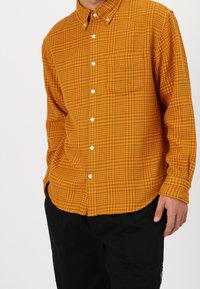 Camicia button-up in un motivo a quadri arancione e giallo, dotata di taschino sul petto e orlo curvo. Realizzata in tessuto testurizzato con bottoni visibili.
