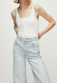 Valkoinen puuvillainen hihaton toppi, joka on yhdistetty vaaleansiniin leveälahkeisiin farkkushortseihin. Topissa on pyöreä kaula-aukko ja ohuet olkaimet. Farkuissa on klassinen napillinen vetskari.