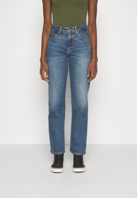 Blauwe denim jeans met een hoge taille, rechte pijpen en vervaagde plekken. Gestyled met zwarte hoge sneakers en een groene top.