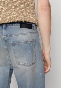 Ljusblå jeans i denim med en blekt finish, med en svart läderlapp vid midjan och två bakfickor.