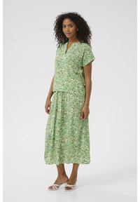 Blommig grön tvådelad outfit som består av en kortärmad topp med V-urringning och en lång kjol. Texturerad tyg med små lövmönster.