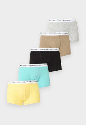Jeune homme musclé debout pieds nus, portant un boxer turquoise avec ceinture Tommy Hilfiger sur fond blanc.