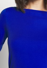 Royal blue angryröd topp, tillverkad av slät tyg. Har en bred halsringning och korta ärmar med en enkel, sömlös design.