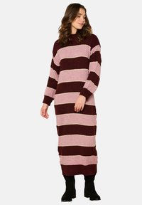Abito in maglia con maniche lunghe, caratterizzato da ampie strisce bordeaux e rosa chiaro, filato testurizzato e orlo a coste. Indossato con stivali neri.