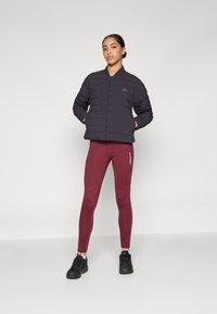 Juodas pūkinis džemperis su horizontaliais siūlais, derinamas su bordo spalvos priglundančiomis legging'ų. Modelis vilki juodus sportinius batelius. Minimalistinis dizainas.