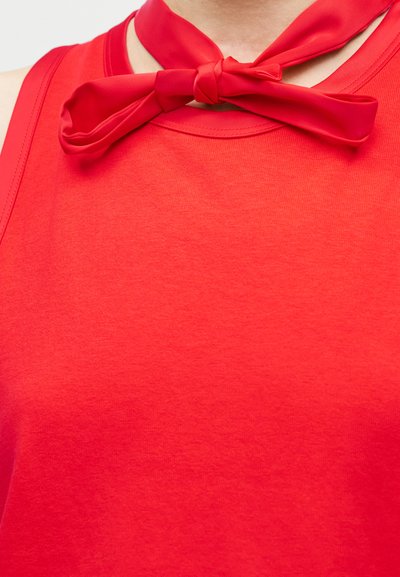 Κοντινό πλάνο ενός ατόμου που φοράει κόκκινο αμάνικο τοπ με κόκκινο υφασμάτινο φιόγκο δεμένο γύρω από τον λαιμό.