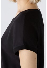 Top corto nero a maniche corte con scollatura tonda. Tessuto liscio e leggero con un design semplice e sottili accenti a coste sulle maniche.