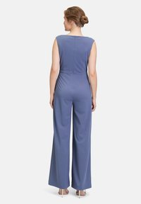 Mouwloze jumpsuit van zacht blauwe stof, met een hoge halslijn, slanke taille en brede pijpen. Met rits aan de achterkant en een gladde textuur.