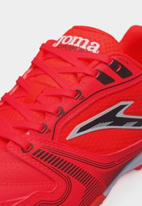 Zapatilla deportiva roja brillante con cordones, logotipo en blanco y negro en el lateral, y parte superior texturizada para ventilación y control.