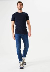 Marineblauw T-shirt met korte mouwen gecombineerd met strakke blauwe spijkerbroek. Schoenen zijn grijs en beige met witte zolen. Eenvoudig ontwerp, minimale details.