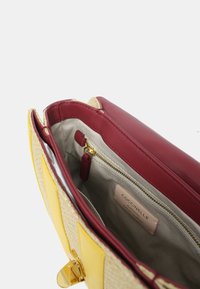 Borsa gialla e paglia con interno borgogna; presenta una tasca con zip, hardware dorato e fodera in tessuto beige. Etichetta con logo all'interno.