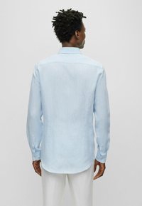 Camicia in lino azzurro chiaro, maniche lunghe, polsini con bottone, texture sottile, orlo posteriore dritto, colletto classico, design minimalista.