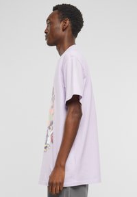 Lilac short-sleeve t-shirt made of cotton, featuring a colorful printed design on the front with various characters and sports elements.