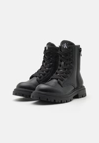 Sorte lær ankle boots med runde tå, snøring foran og glidelås på siden. Har robuste såler og subtil merking på tungen.