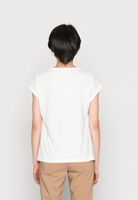 White cotton t-shirt with rolled cap sleeves, a relaxed fit, and a rounded neckline, paired with beige trousers. Simple and clean design.