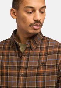 Bruin geruite overhemd met oranje en blauwe strepen, met een button-down kraag, textuurstof en een klein logo op de borst. De knopen zijn donker.