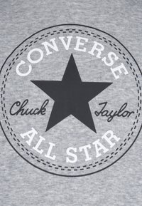 Tela gris con una estrella negra y el texto "Converse" y "Chuck Taylor" en blanco, enmarcada por un diseño de círculo de líneas discontinuas.
